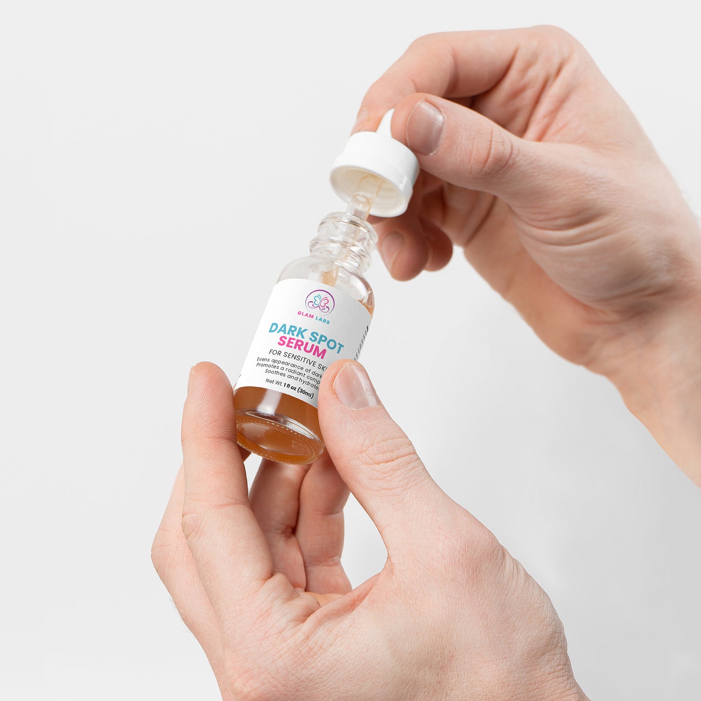 Glam Labs Dark Spot Serum for Sensitive Skin bottle with dropper held by hands on white background